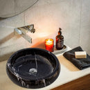 Toros Black Marble Above Vanity Bathroom Vessel Sink Polished (D)16" (H)5" bathroom linstalled above travertine vanity and chrome wall mount modern faucet along with dark gray hand-towel liquid soap dispenser and candle inside orange glass