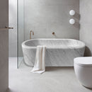 Imperial White Marble Bathtub Hand-carved from Solid Marble Block (W)32" (L)70" (H)20" installed bathroom gray porcelain tile on walls and floor glass side door gold faucet and white towel on the tub
