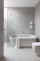 Imperial White Marble Bathtub Hand-carved from Solid Marble Block (W)32" (L)70" (H)20" installed bathroom gray porcelain tile on walls and floor glass side door gold faucet and white towel on the tub wide view