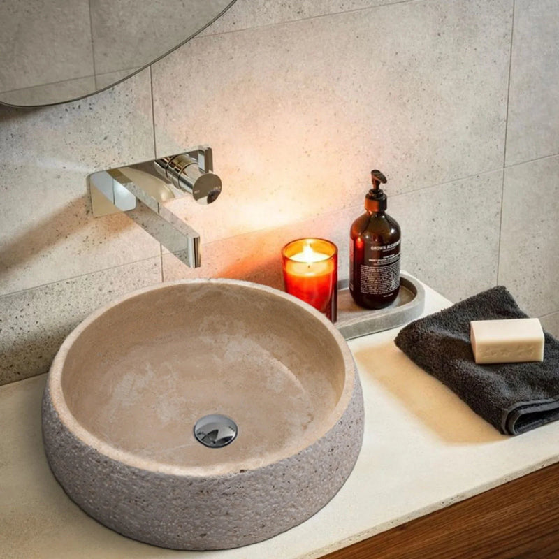 Light Beige Travertine Above Vanity Bathroom Sink Rustic Outside (D)16" (H)6" installed bathroom chrome wall mount faucet candle inside orange glass and liquid soap dispenser with dark gray and soap on the stone vanity