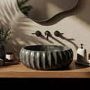 Marble sink with black fixtures on a wooden vanity, surrounded by plants and bathroom items.