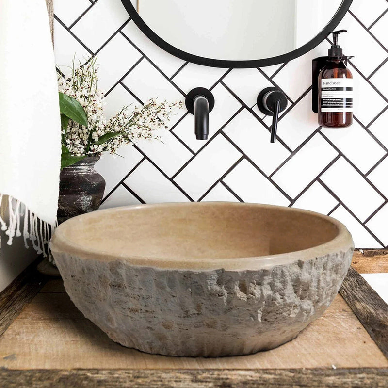 Troia Light Beige Travertine Above Vanity Bathroom Sink Dragon Split-face Exterior (D)16" (H)6" bathroom view installed above wooden vanity and white herringbone wall tiles and black wall-mount faucet hand-liquid soap mounted on wall and round black framed mirror