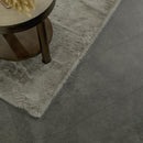 Gray rug on a dark tiled floor with a wooden side table corner.