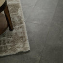 Close-up of a textured rug on a tiled floor with a wooden chair leg visible.