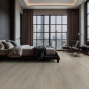 Modern bedroom with large windows offering a cityscape view, featuring a bed and armchairs.