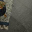 Dark gray tiles with a textured rug and decorative item on a wooden surface