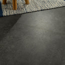 Close-up of dark gray tiles with a textured surface, partially covered by a patterned rug.