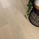 Close-up of light wood flooring with a plant and black woven basket in the corner.