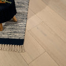 Close-up of herringbone wooden flooring with a rug and plant in the corner.